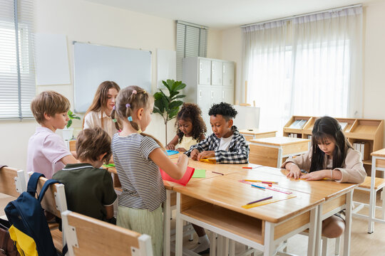 Happy diverse group of primary school children doing arts and crafts in a classroom, Teacher and elementary students engaging in a creative paper craft project, Education concept