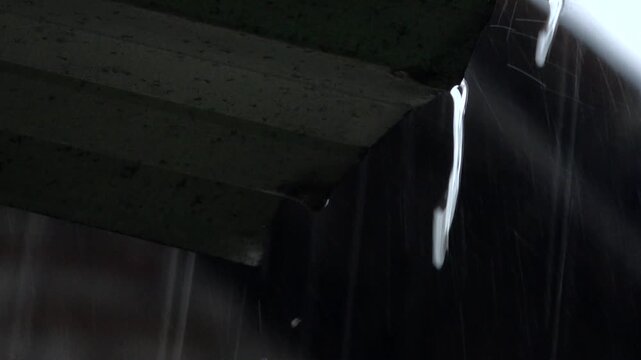 A close up shot of torrential monsoon rain pouring and streaming heavily off the edge of a corrugated awning canopy roof during a storm.
