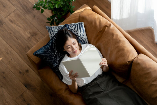 ソファーに寝転び本を読む40代日本人女性