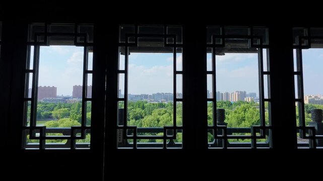 View from an interior space with traditional window frames, overlooking lush greenery and distant urban buildings under a clear sky.
