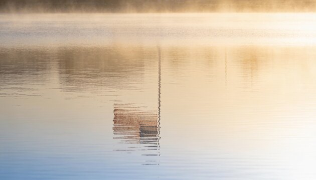 Serene Morning Mist on Water: A calm lake surface reflects the soft, golden hues of early morning light filtering through a gentle mist, creating an atmosphere of tranquility.