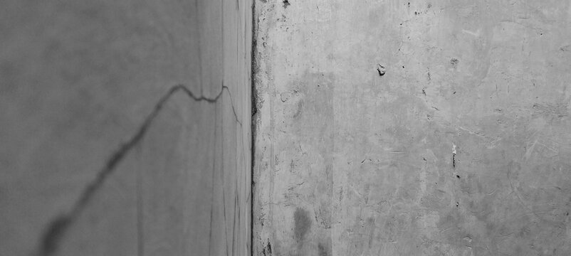 A black-and-white concrete wall corner featuring cracks and a weathered cement texture.