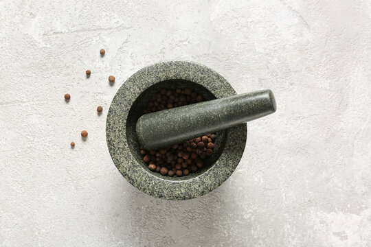Stone mortar and pestle with whole allspice on white surface