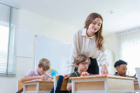 Teacher guiding elementary student with schoolwork in the classroom, Young female teacher helping young student with lesson at school desk, Education concepts