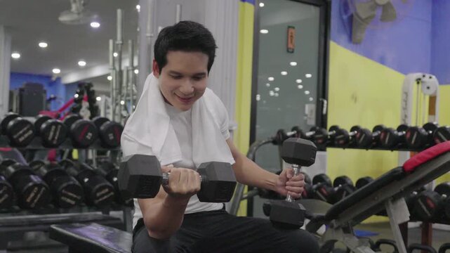 Handsome young Asian man doing single-arm dumbbell row exercise on a bench at the gym