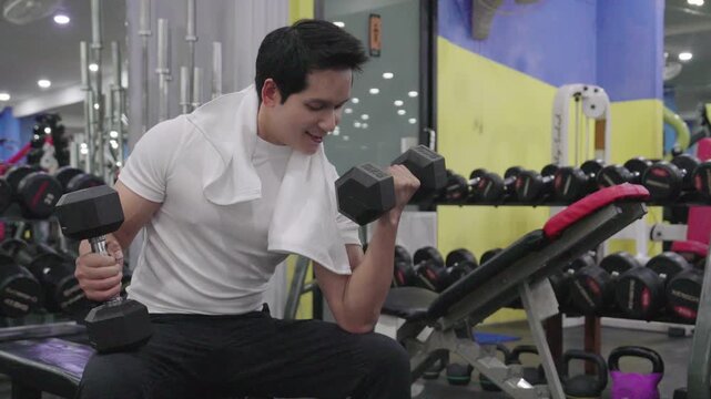 Handsome young Asian man doing single-arm dumbbell row exercise on a bench at the gym