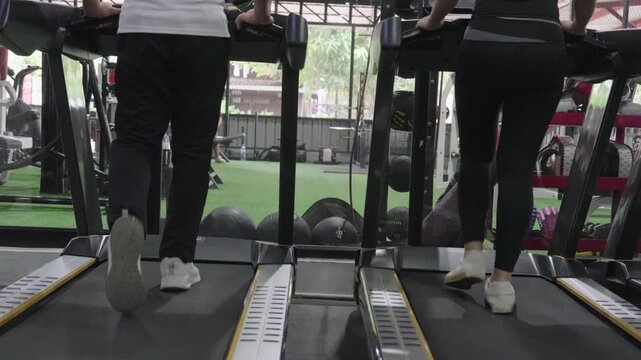 A friendly male trainer is setting up the treadmill display for an Asian woman exercising in a modern gym.