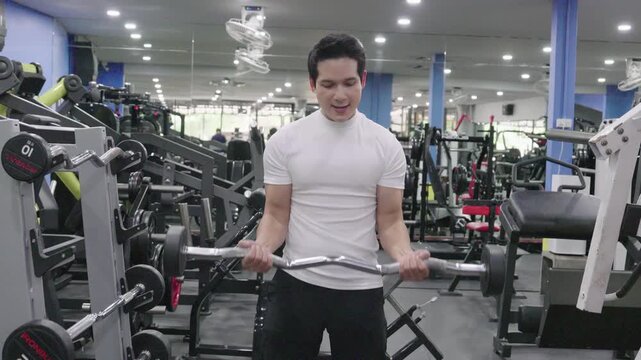 Strong young Asian man lifting barbell on bench press machine with the assistance of a female trainer at the gym.