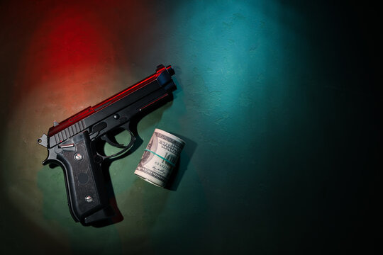 Black handgun and roll of US dollar bills on textured surface