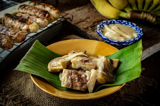 Traditional Thai grilled bananas with sweet coconut milk dipping sauce served on a plate with banana leaf, popular Asian street food dessert and sweet afternoon snack lifestyle concept.