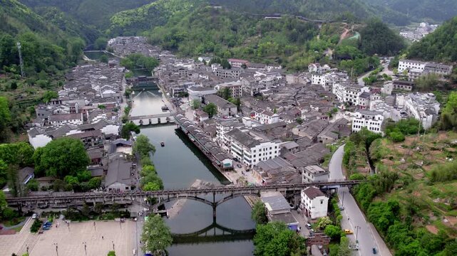 Aerial view of a traditional riverside town with multiple bridges, nestled among green hills and dense buildings.