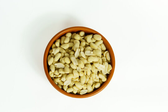 Top view of a terracotta bowl filled with roasted peeled peanuts, isolated on white background