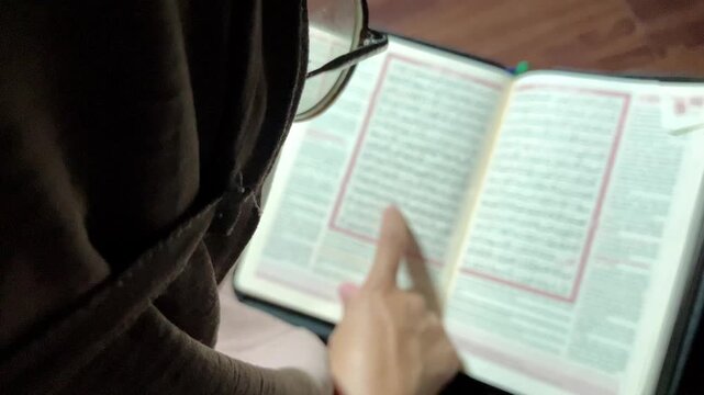 4K slow motion static over the shoulder shot of a young muslim woman in hijab with selective focus blur background reading holy Quran book Authentic Islamic spiritual broll for documentary use