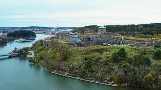 Bohus Fortress aerial drone view of a medieval stone castle situated on a cliff above the river in Kung&auml;lv, Sweden, surrounded by vibrant autumn trees.