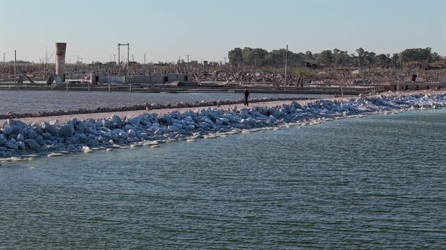 Man walking beside salt-covered ruins of Villa Epecuen on Lake Epecuen in Adolfo Alsina, Buenos Aires Province, Argentina, site of the catastrophic 1985 flood, drone oblique pullback tracking shot.