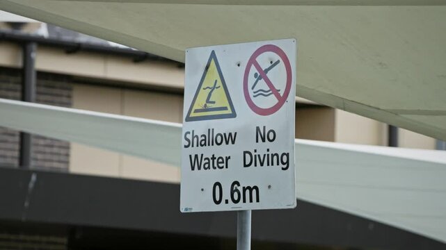 Safety sign warning of shallow water depth and prohibiting diving at a public swimming pool. Sign indicates water depth of 0.6 metres and highlights aquatic safety regulations. Close up.