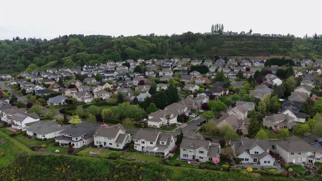 Affluent suburban neighborhood with large single-family homes, solar panels and curved streets nestled against a densely forested hillside in Tacoma, Washington, USA. Aerial drone view.