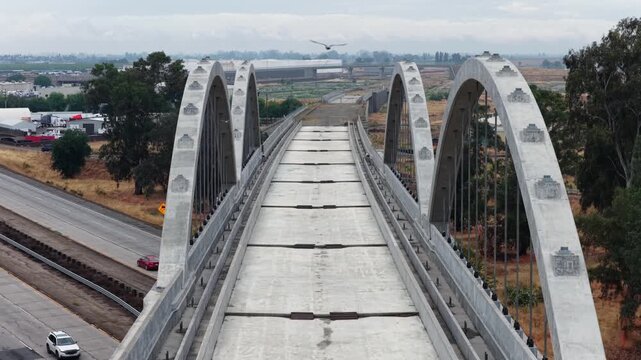 Cedar Viaduct high-speed rail arched bridge deck stretches over dry Central Valley terrain with freeway and agricultural flatlands below in Fresno, California, USA. Aerial drone view.