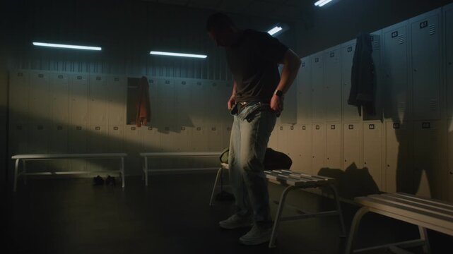 Focused Male Athlete With Prosthetic Leg Near White Bench Removes Denim Pants to Prepare for Training in Modern, Atmospheric Dressing Room. Concept of Preparation, Breaking Barriers in Sports.