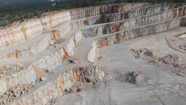 Aerial view of a large open-pit quarry mine with terraced rock walls, exposed stone layers, and dusty ground surfaces in Portugal.