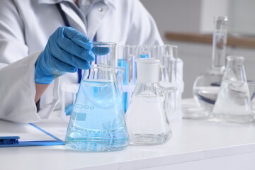 Fototapeta premium Female scientist with flasks of water samples at table in laboratory, closeup