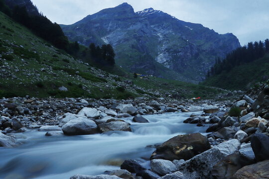 hampta river flowing through the lush green mountain valley, chika campsite area, hampta pass trek, kullu valley near manali, himachal pradesh, india