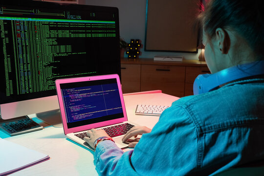 Female programmer working with laptop in office at night, back view