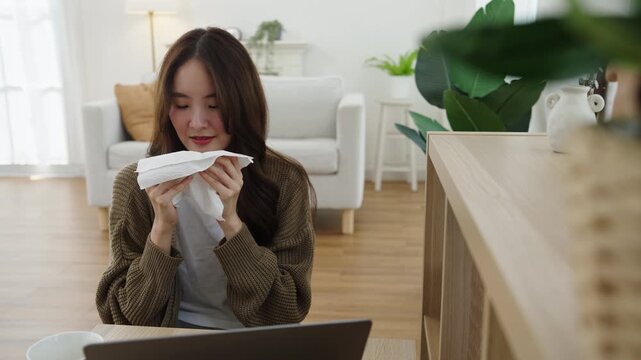 Young woman blows her nose with a tissue at home while recovering from a cold, highlighting seasonal illness and personal hygiene.