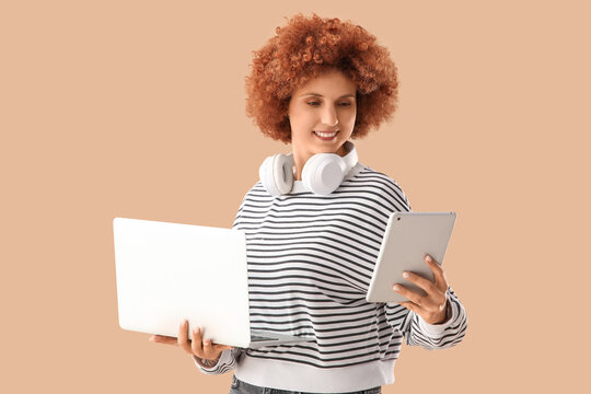 Young female programmer with laptop and tablet computer on beige background