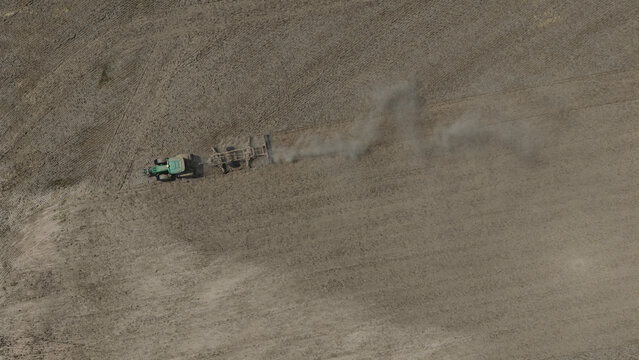 Aerial view of a tractor plowing a dry field and creating a trail of dust in Portugal.