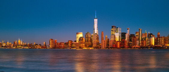 Obraz premium New York City panorama skyline. New York Freedom Tower glowing near NYC panorama. New York riverfront panorama at dusk. New York panoramic scene.