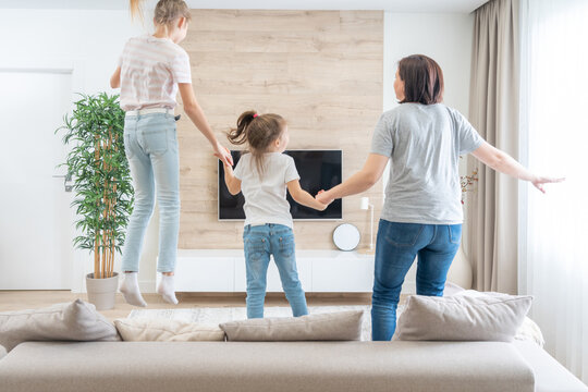 Mother and two daughters having fun jumping on a sofa in living room