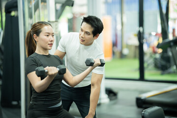 Fototapeta premium A young woman is performing weight training at the gym, lifting weights with determination to improve her physical performance, balance, and endurance, while building muscle and maintaining he