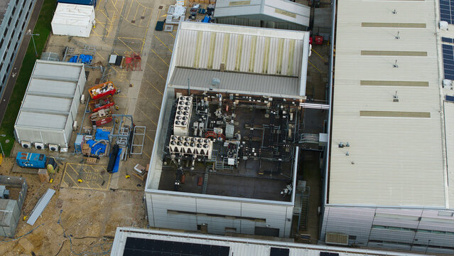 Aerial view of industrial ventilation and cooling fans on a flat roof with complex piping and metal structures in an industrial facility in Stevenage, England, United Kingdom.