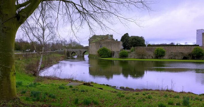 Wide landscape view featuring Leeds Castle, its moat and stone bridge surrounded by tranquil grounds.