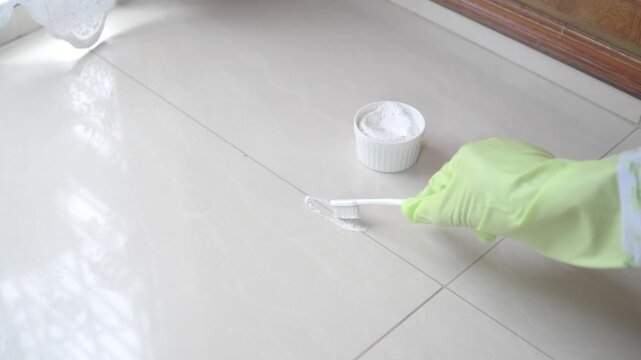 Person Cleaning Tile Grout with Toothbrush and Cleaning Powder