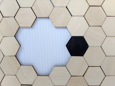Hexagonal wooden puzzle tiles form a honeycomb pattern with central gap and contrasting black tile highlighting geometric symmetry