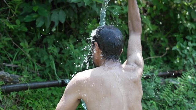 Man bathing under a refreshing natural water stream in forest