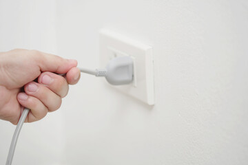 Naklejka premium close up hand plugging adapter Electrical appliances with outlet socket plug ,electric safety concept