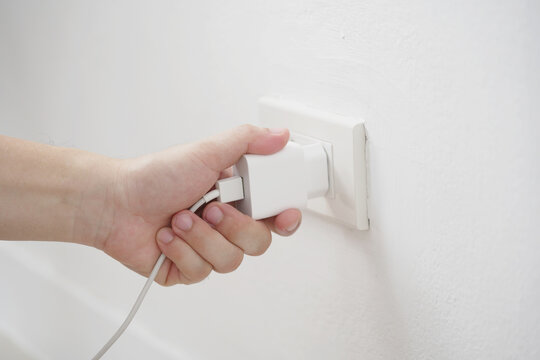 close up hand plugging adapter charge the battery with outlet socket plug and hold mobile phone on wall ,electric safety concept