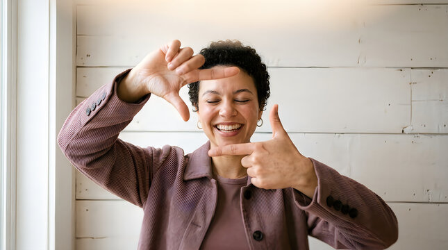 Happy young woman making a picture frame gesture with her hands and smiling at the camera in a bright indoor room