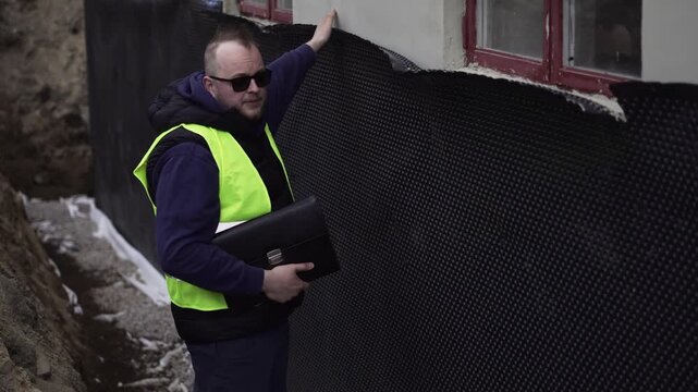Construction inspector reviews exterior wall damage and points out defects during a site inspection, ideal for renovation, quality control, and building safety visuals.