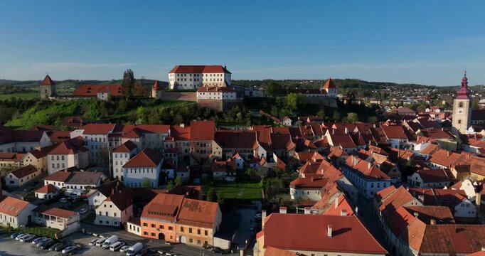 Reveal aerial shot the red rooftops of Ptuj Old Town and Ptuj Castle overlooking the historic city in Slovenia. Daytime drone aerial
