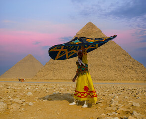 Fototapeta premium Vibrant Egyptian tanoura dancer twirling a colorful folklore skirt overhead before the Giza pyramids under a pink twilight sky ideal for Egypt travel