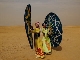 Fototapeta premium Two energetic Egyptian Tanoura folk dancers performing with colorful star patterned spinning skirts in the desert near the Giza pyramids ideal for
