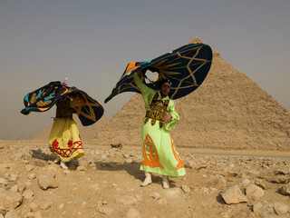 Fototapeta premium Two Egyptian Tanoura folk dancers spinning vibrant colorful skirts overhead in an energetic whirling performance before the ancient Giza pyramids