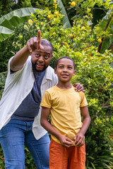 Diverse father pointing and guiding son in backyard, son holding small leaf near lemon tree © wavebreak3