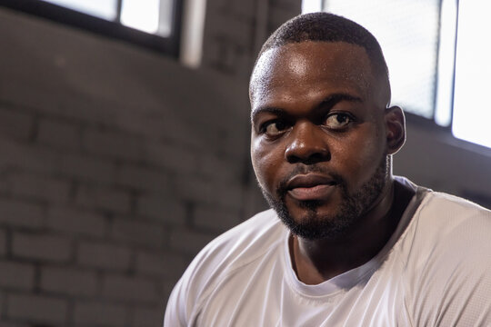 Resting after intense training, man wearing white athletic T-shirt sweating in gym by block wall