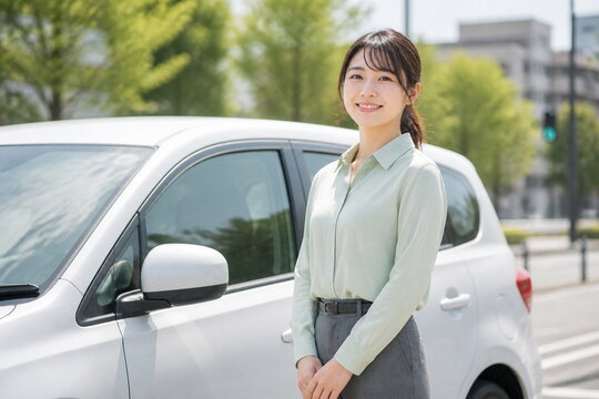 コンパクトカー横で微笑む若い女性スタッフ