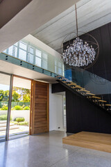 Obraz premium Floating staircase cantilevering from dark wall with glass rail, pivot door opening to yard